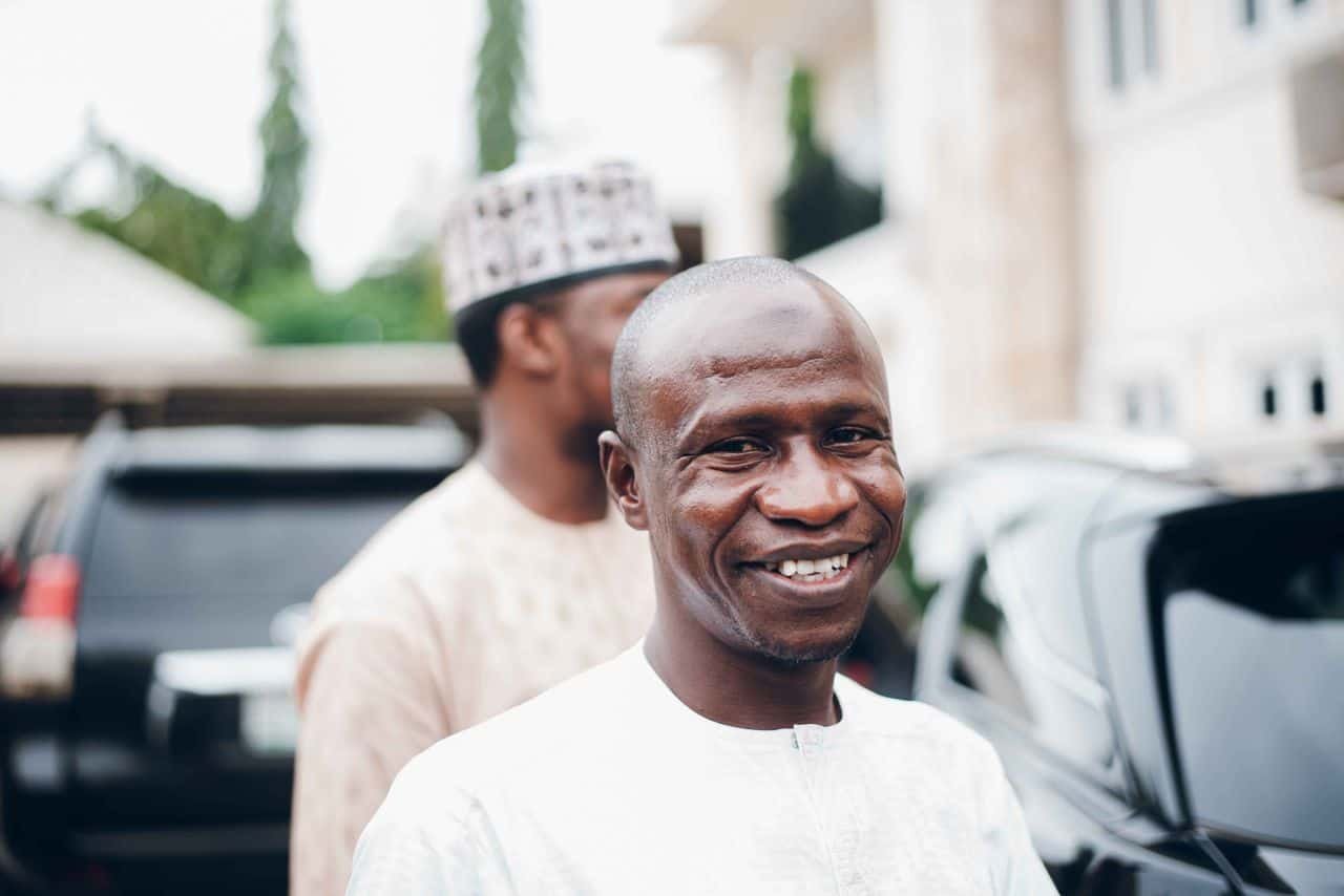 Smiling adult man dressed in traditional clothing outside in an urban environment.